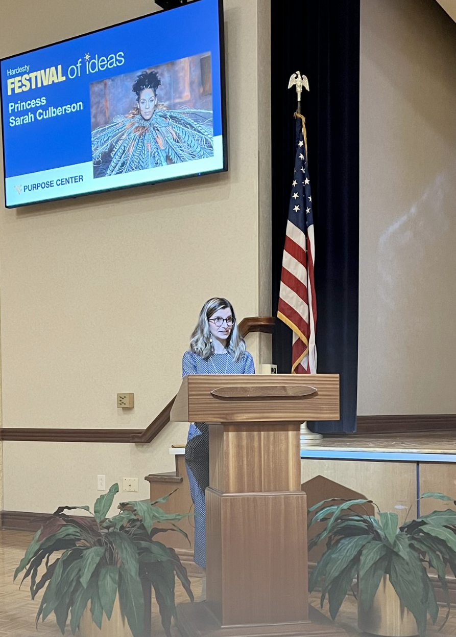 Presidential Student Ambassador Giana Loretta introduced Princess Sarah Culberson at the Hardesty Festival of Ideas/Purpose Week event at the WVU Mountainlair.  Giana is standing at a podium giving an introduction.